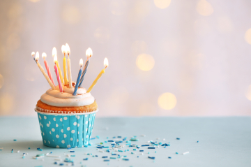 Cupcake mit bunten Geburtstagskerzen, Konfetti und Glitzer.